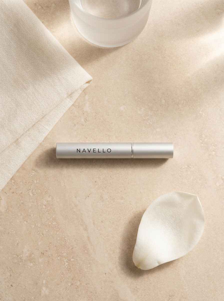 The Navello tube on a travertine surface beside folded linen, a glass of water and a white petal.